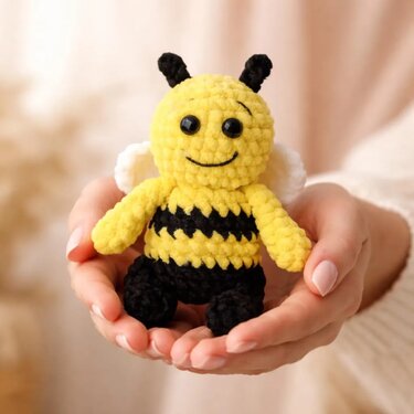 Gehäkelte Amigurumi-Biene, gelb und schwarz gestreift, mit weißen Flügeln, gehalten in zwei Händen
