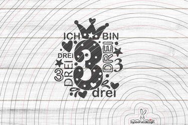 Schwarzes Plottmotiv „Ich bin DREI“ mit gepunkteter Zahl 3, Krone, Herzen und Sternen vor hellem Holzbrett-Hintergrund.