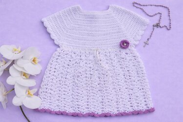 Festliches weißes gehäkeltes Babykleid mit lila Blüte, Orchideen und Perlenkette