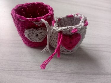 Zwei kleine gehäkelte Säckchen: pinkes mit grauem Herz und graues mit pinkem Herz, jeweils mit Kordelzug
