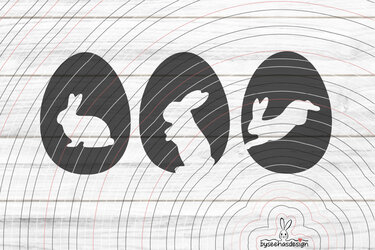 Drei Hasen‑Silhouetten in Ei‑Form auf weißer Holzoberfläche