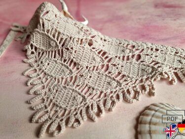 Beige crocheted triangle shawl with leaf lace panels and looped fringe on pink background