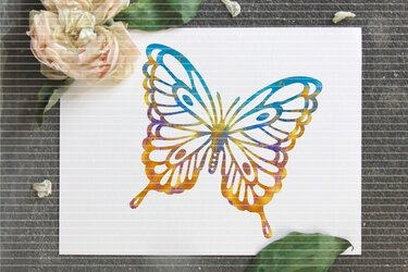 Stilisierter Schmetterling mit filigranen Flügeln und blau‑violett‑goldenem Farbverlauf auf weißem Papier, mit Blumen am Rand.