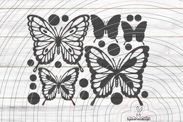 Vier schwarze Schmetterlingsmotive, teils filigran, teils als Silhouette, begleitet von dekorativen Punkten auf hellem Holzuntergrund; kleines Hasen-Wasserzeichen in der Ecke.