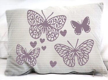 Vier violette Schmetterlingssilhouetten mit unterschiedlichen Mustern und mehrere kleine Herzen auf einem Kissen