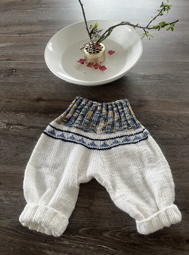Gestrickte weiße Babyhose mit buntem Musterbund und gerippten Bündchen