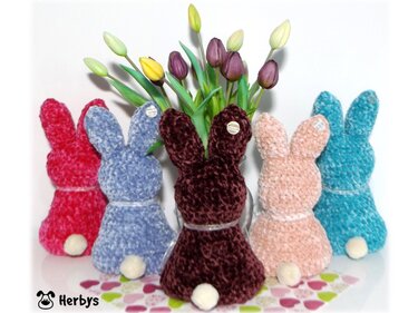 Fünf flauschige gehäkelte Hasen in verschiedenen Farben vor Tulpen