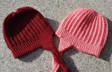 Handgestrickte Baby-Ohrenklappenmützen in Rosa und Bordeaux mit gleichmäßigem Rippenmuster nebeneinander