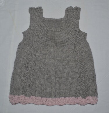 Gestricktes graues Baby- und Kinderkleid, ärmellos, quadratischer Ausschnitt, seitliche Musterstreifen und rosa gewellter Saum
