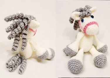 Weißes Amigurumi-Pferd mit grauer lockiger Mähne, grauen Hufen, blauen Augen und pinkem Zaumzeug.