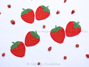Sechs gehäkelte Erdbeer-Topflappen mit grünen Blättern und gelben Punkten auf weißem Hintergrund, umgeben von frischen Erdbeeren.