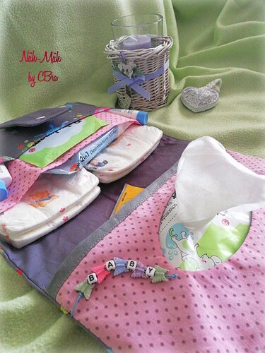 Aufgeklapptes rosa Wickel-Utensilo mit Pünktchenmuster, gefüllt mit Windeln, Feuchttüchern und Pflegeprodukten auf einer grünen Decke.