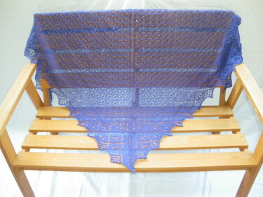 Blaues gestricktes Dreieckstuch mit Spitzendetails, über eine Holzbank gelegt.