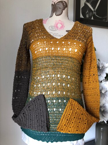 Mehrfarbige gehäkelte Damen‑Tunika in Senf, Grün und Grau mit V‑Ausschnitt, Lochmuster und dreieckigen Saumblenden auf Schaufensterpuppe