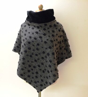 Grauer Poncho mit schwarzen Punkten und breitem schwarzen Rollkragen auf einer Schneiderpuppe