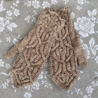 Beige fingerlose Handschuhe mit detailliertem Zopfmuster auf grauem Stoff mit Blumenmuster