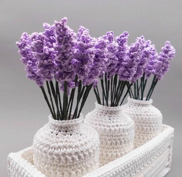 Three crocheted white vases with purple yarn flower stems arranged in a rectangular tray