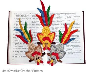 Drei gehäkelte Hähnchen-Lesezeichen mit bunten Schwänzen auf einem aufgeschlagenen Buch