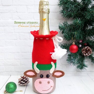 Gehäkelte Flaschenhülle in Rot, Grün und Beige mit Kuhgesicht vor weihnachtlicher Dekoration