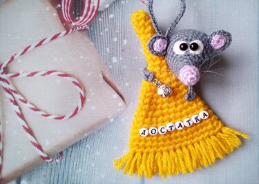 Gehäkelte graue Amigurumi-Maus in gelbem Fransenanhänger neben Geschenkbox