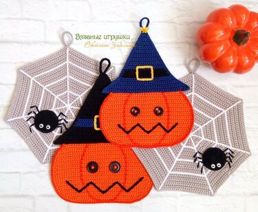 Gehäkelte orange Kürbisse mit blauen Hexenhüten neben hellgrauen Spinnennetz-Topflappen mit schwarzen Spinnen