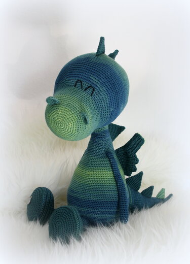 Gehäkelter sitzender Amigurumi-Drache in blau-grünem Farbverlauf, seitliche Ansicht