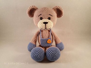 Beiger sitzender Amigurumi-Teddybär mit blauer Latzhose