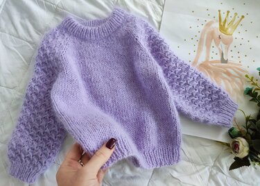 Lilafarbener Strickpullover für Kleinkinder mit glatt gestricktem Rumpf und strukturierten Ärmeln, an der Vorderkante leicht gehalten.