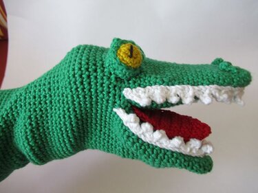 Nahaufnahme einer gehäkelten grünen Krokodil-Fingerpuppe mit weißen Zähnen