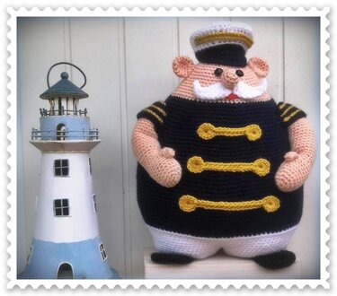 Gehäkelte Kapitänsfigur in schwarzer Uniform neben Modell-Leuchtturm