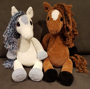 Zwei gehäkelte Amigurumi-Pferde sitzend: weißes Fantasiepferd und braunes Pferd