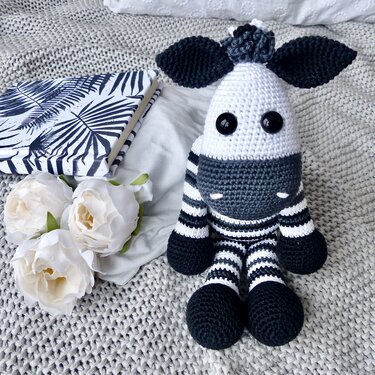 Handgehäkeltes Amigurumi‑Zebra in Schwarz und Weiß mit langen Beinen auf gestrickter Decke