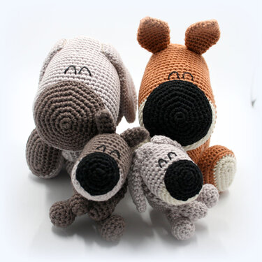 Vier gehäkelte Amigurumi-Hunde in Braun- und Grautönen, zwei größere hinten, zwei kleinere vorn.