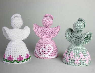 Drei gehäkelte Amigurumi-Engel in Weiß, Rosa und Grün mit Rüschenflügeln