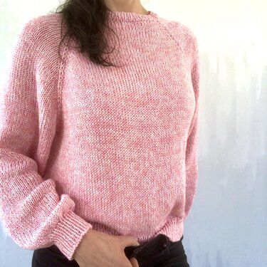 Person trägt einen melierten rosa Strickpullover mit Raglanärmeln und Rundhalsausschnitt.