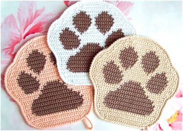 Drei gehäkelte Topflappen in Pastellfarben mit braunen Pfotenmotiven