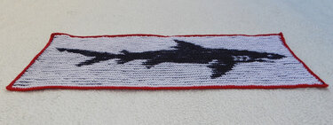 Gestrickter rechteckiger Überwurf mit schwarzem Haifisch auf weißem Hintergrund und rotem Rand