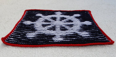 Gestricktes rechteckiges Panel mit weißem Totenkopf auf schwarzem Hintergrund und rotem Rand