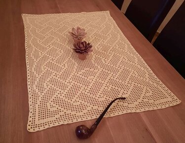 Rechteckiger gehäkelter Filet-Tischläufer in Creme auf Holztisch, dekoriert mit zwei Blüten