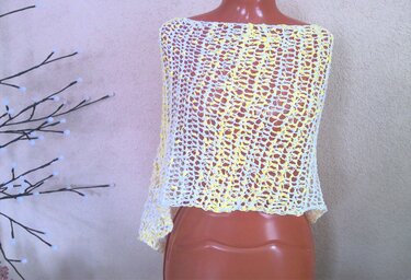 Gelb-weißer gehäkelter Damenponcho mit offenem Netzmuster auf Schaufensterpuppe