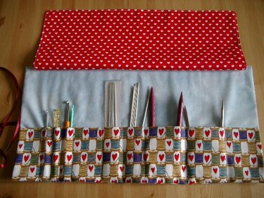 Rollbares Utensilo mit Einsteckfächern, roten Herzen auf Klappe und gemustertem Garnspulenstoff, bestückt mit Häkelnadeln und Stricknadeln