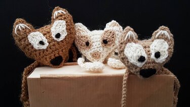 Drei gehäkelte Fuchs-Lesezeichen in Braun- und Beigetönen an einer Kartonkante hängend