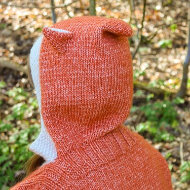 Rückansicht einer orange-melierten gestrickten Kinderkapuze mit kleinen Ohren und geripptem Halsbund