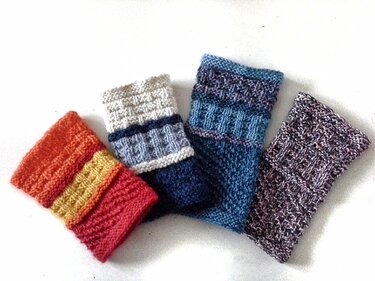 Nahaufnahme von vier gestrickten Armstulpen mit verschiedenen Zopf- und Strukturmustern.