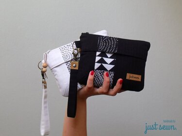 Zwei flache Kosmetiktaschen in Schwarz und Weiß mit Reißverschluss, Karabiner und Handgelenkschlaufe, eine wird gehalten