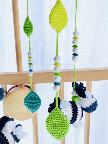 Gehäkeltes Mobile mit grünen und türkisfarbenen Blättern, weißen, grünen und türkisfarbenen Perlen und gestreiften Tieranhängern an Holzlatten eines Babybetts