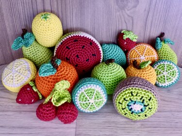 Gehäkelte Früchte wie Melone, Kiwi, Orange, Zitrone, Erdbeere und Kirschen auf hellem Holzuntergrund