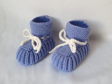 Hellblaue gestrickte Babyschuhe mit Rippenfuß, weißen Schnürbändern und hohem Schaft