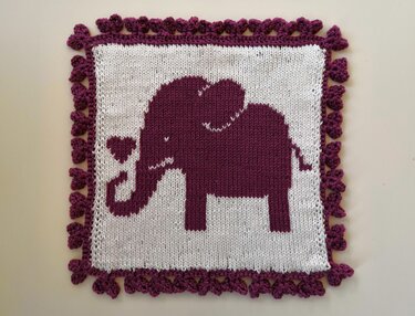 Quadratisches Strickstück in Weiß und Dunkelviolett mit Elefantenmotiv und dekorativem Rand