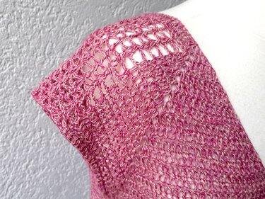 Nahaufnahme des Maschenbilds eines gehäkelten rosa Kurzarm-Shirts an der Schulter